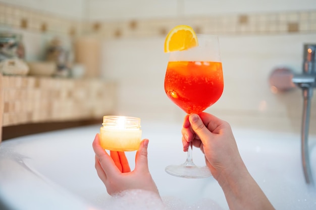 Frau mit Glas Aperol Spritz oder Cocktail im Bad mit Aromakerze