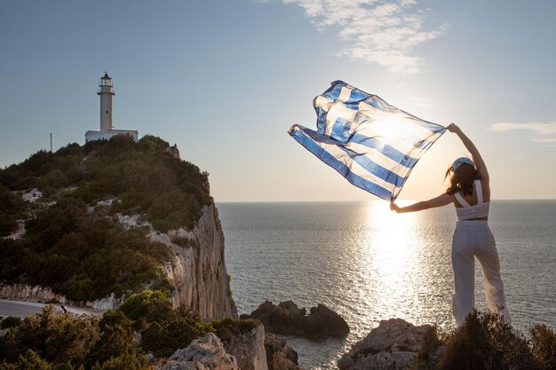 Frau mit griechischer Flagge, die den Sonnenuntergang über dem Meer betrachtet