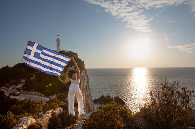 Frau mit griechischer Flagge schaut auf den Sonnenuntergang über dem Meer