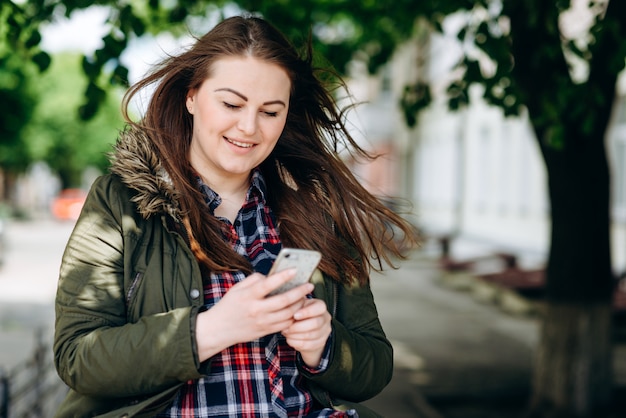 Frau mit grüner Jacke im Park mit Handy