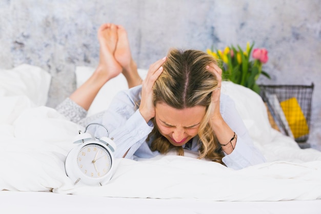 Foto frau mit händen, die ihre ohren bedecken, liegt zu hause auf dem bett an der wand