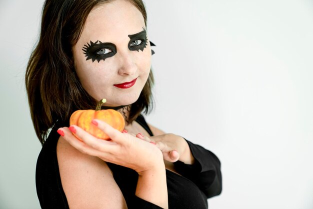 Frau mit Halloween-Make-up im Gesicht hält Kürbis in der Hand.