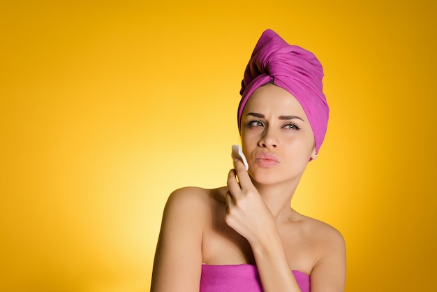 Frau mit Handtuch auf dem Kopf entfernt Make-up mit einer Baumwollscheibe