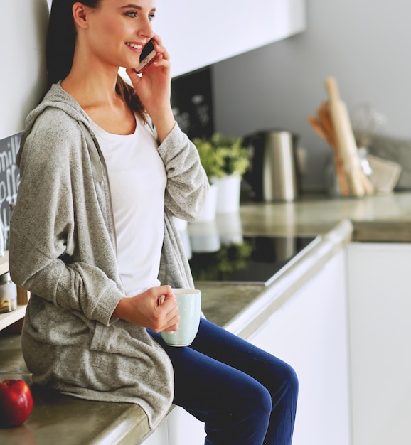 Frau mit Handy sitzt in moderner Küche