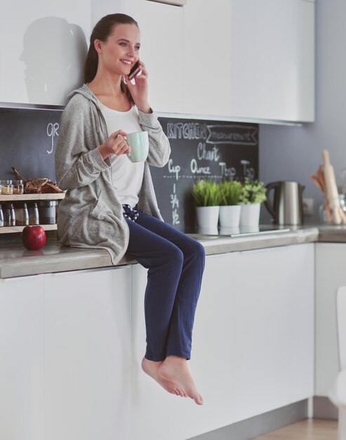 Frau mit Handy sitzt in moderner Küche