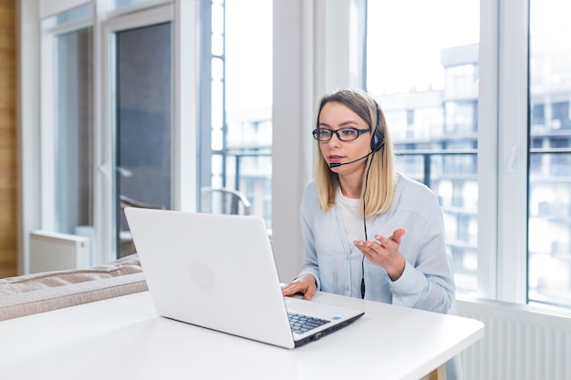 Frau mit Headset und Brille kommuniziert mit Kunden aus der Entfernung eines Laptops