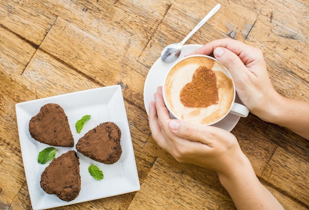 Frau mit heißer Tasse Kaffee und Schokoladenkuchen in Herzform