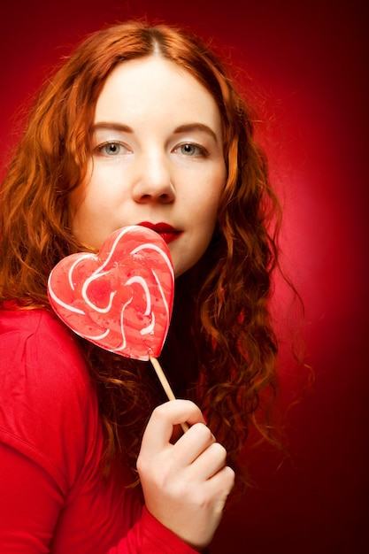 Frau mit Herzkaramell über rotem Hintergrund