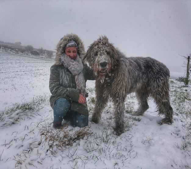 Frau mit Hund sitzt während des Schneefalls auf dem Schnee