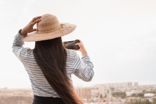 Frau mit Hut, die im Sommer im Freien per Telefon fotografiert