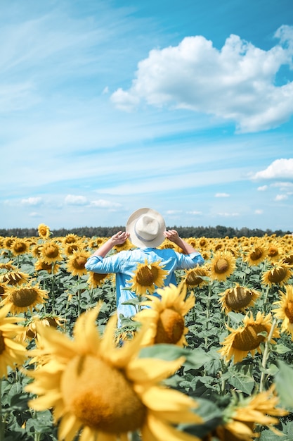 Frau mit Hut im Sonnenblumenfeld, die die Natur genießt