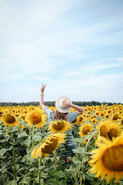 Frau mit Hut im Sonnenblumenfeld, die die Natur genießt