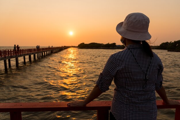 Frau mit Hut steht mit Blick auf den Sonnenuntergang am Strand gegen den goldenen Sonnenuntergang.