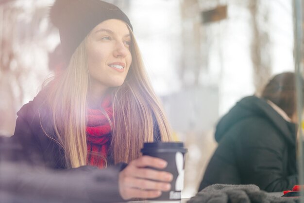 Frau mit Hut trinkt Kaffee in einem Coffeeshop hinter dem Glas