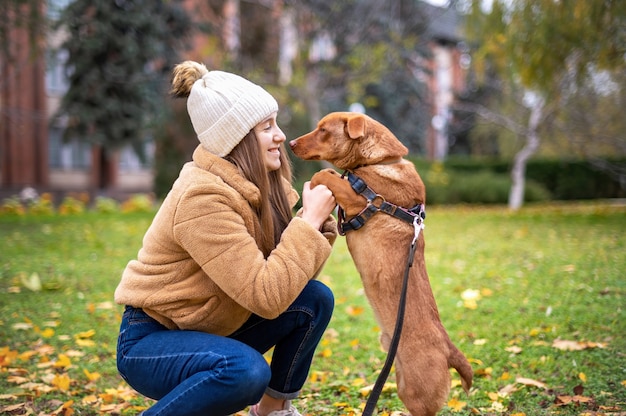 Frau mit ihrem Hund im Herbst in einem Park. Hundepfoten in Frauenhänden, sie schaut es an und lächelt.