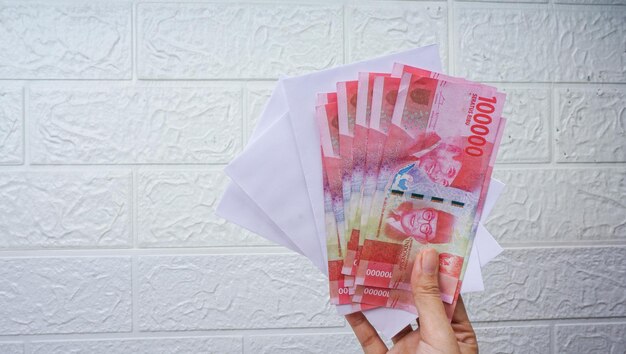 Frau mit indonesischen Banknoten mit weißem Umschlag Rupiah-Währungskonzept gegen weiße Wand