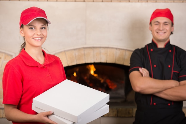 Frau mit Kästen Pizza in der roten Uniform und im Chef im Schwarzen.