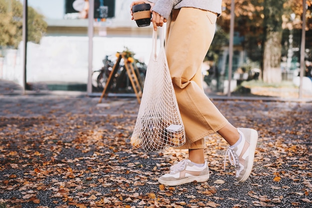 Frau mit Kauf in wiederverwendbarer Netztasche aus Baumwolle auf Schaufensterhintergrund des Zero-Waste-Shops