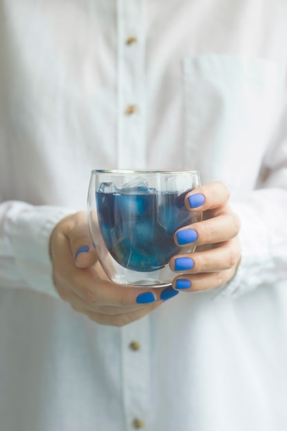 Frau mit klassischer blauer Maniküre hält ein Glas Matcha-Blautee