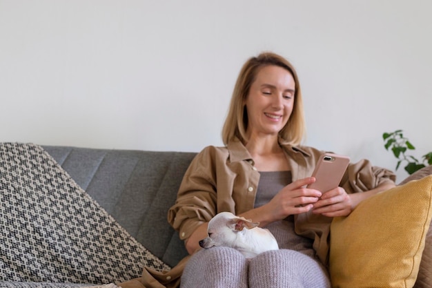 Frau mit kleinem Hund auf dem Schoß, die mit dem Telefon auf der Couch sitzt