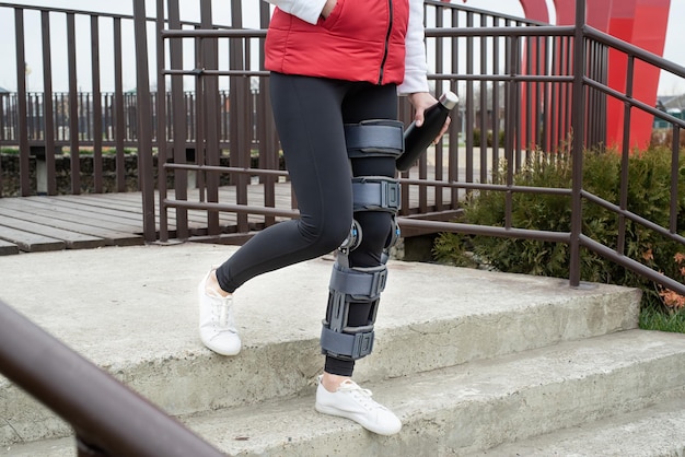Frau mit Knieorthese oder Orthese nach einer Beinoperation im Park