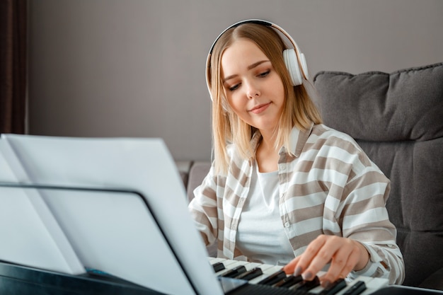 Frau mit Kopfhörern, die Klaviermusik auf Synthesizer aus Noten spielt. Teenager Mädchen Musiker Pianist verbessert die Fähigkeiten, Klavier zu spielen. Musikpädagogik Hobby Gesang singen mit Musikinstrument Klavier.