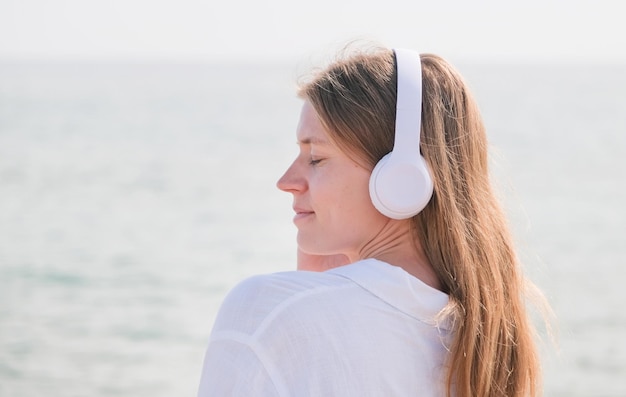 Frau mit Kopfhörern hört Musik, atmet frische Luft und entspannt sich am Strand