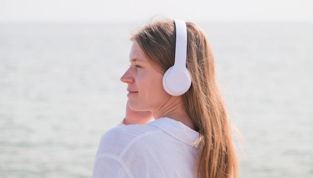 Frau mit Kopfhörern hört Musik, atmet frische Luft und entspannt sich am Strand