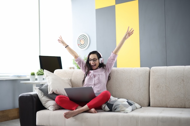 Frau mit Kopfhörern sitzt auf Couch mit Laptop