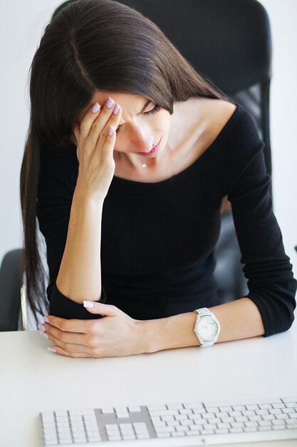 Frau mit Kopfschmerzen sitzt am Tisch im Büro
