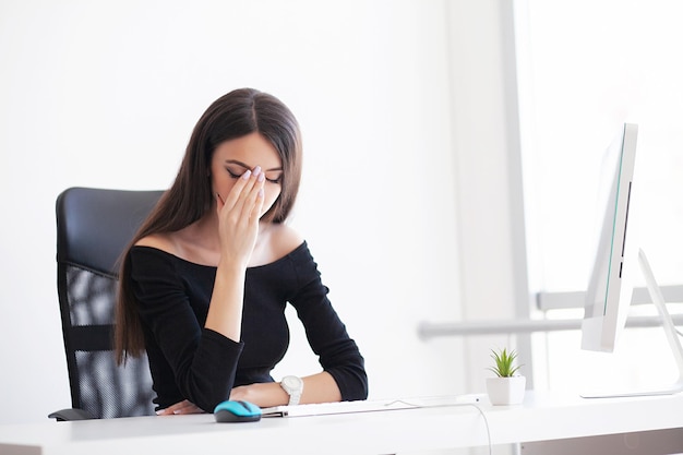 Frau mit Kopfschmerzen sitzt am Tisch im Büro