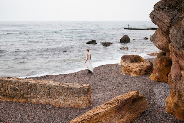 Frau mit kurzem Haarschnitt und Kleid in der Nähe von Meer und Felsen im Herbst