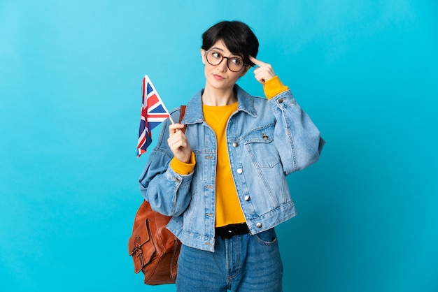 Frau mit kurzen Haaren, die eine Flagge des Vereinigten Königreichs lokalisiert auf blauem Raum hält, der Zweifel und Denken hat