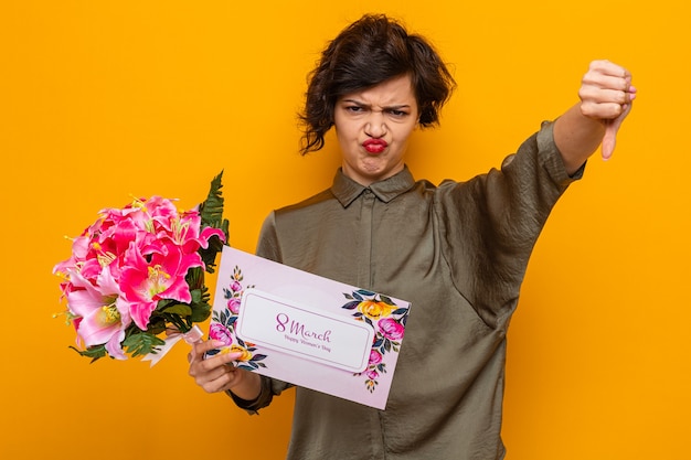 Frau mit kurzen Haaren, die Grußkarte und Blumenstrauß hält, die unzufrieden aussehen und Daumen nach unten zeigen, um den internationalen Frauentag am 8. März zu feiern