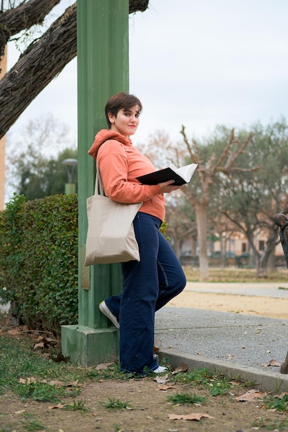 Frau mit kurzen Haaren, die mit einem Buch in der Hand in die Kamera schaut