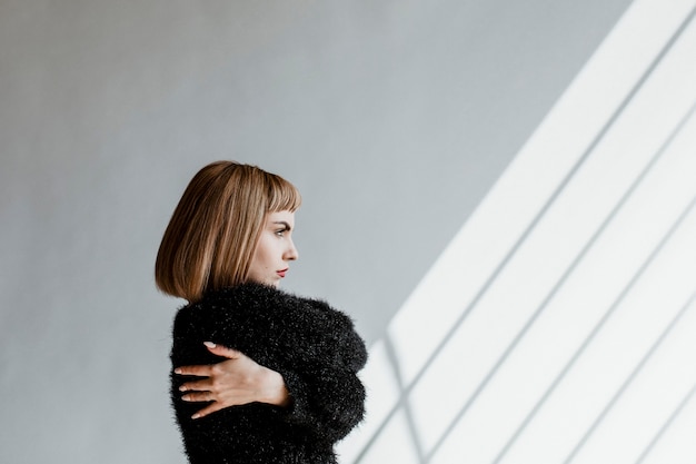 Frau mit kurzen Haaren in einem schwarzen, flauschigen Pullover, die sich umarmt