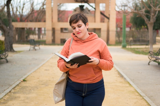 Frau mit kurzen Haaren liest ein Buch und lächelt in einem Park