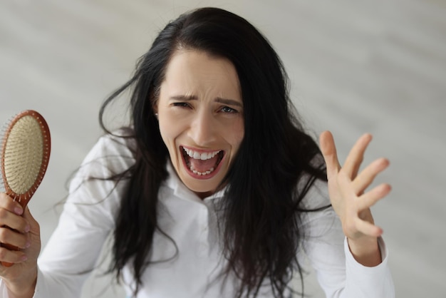 Frau mit langen Haaren schreit und hält Kamm in den Händen Haarausfallprobleme nach vorheriger