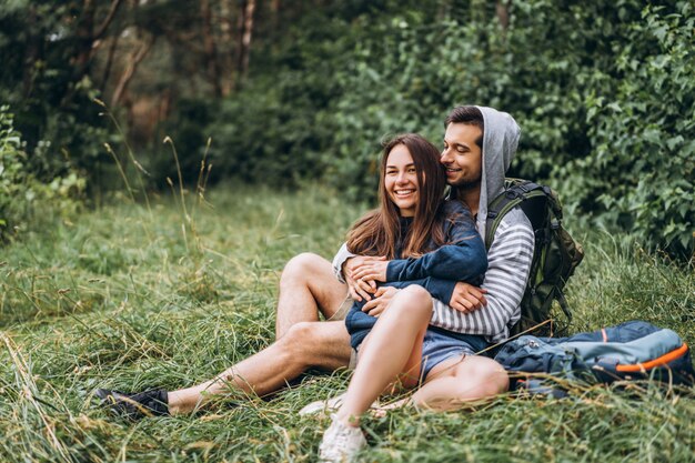 Frau mit langen Haaren und Mann, die auf dem Gras im Wald mit Rucksäcken sitzen. Viel Spaß in der Natur, umarmen und küssen