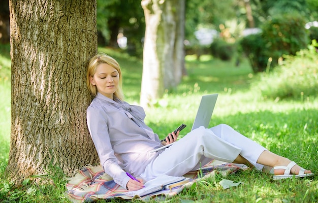 Frau mit Laptop-Computer arbeiten im Freien auf Baumstamm lehnen Mädchen arbeiten mit Laptop im Park sitzen auf Gras Natürliche Umwelt Büro Arbeit im Freien Vorteile Bildungstechnologie und Internet-Konzept