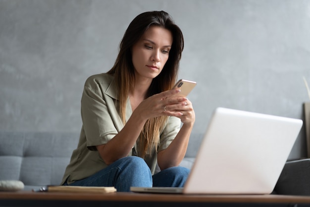 Frau mit Laptop und Handy auf dem Sofa.