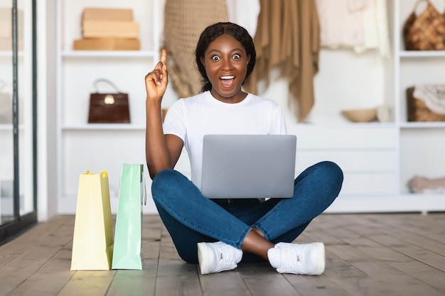 Frau mit Laptop zeigt mit dem Finger nach oben und hat Ideen beim Indoor-Shopping