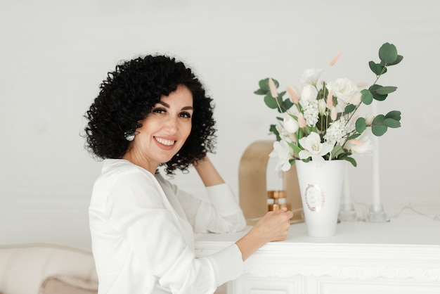 Frau mit lockigem Haar und einem schneeweißen Lächeln steht neben einem Blumenstrauß