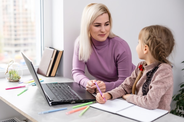 Frau mit Mädchen macht Hausaufgaben am Laptop