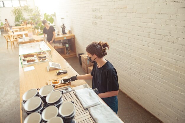 Frau mit Maske, die Barista im Kaffeehaus arbeitet