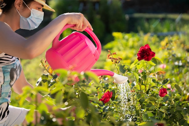 Frau mit Maske, die Blumen wässert