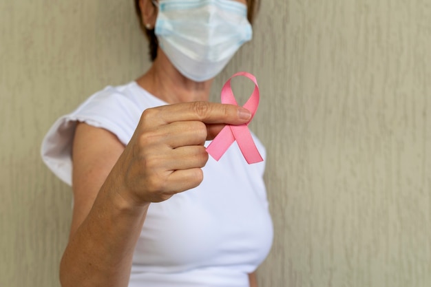 Frau mit Maske hält rosa Schleife in der Hand Brustkrebs-Präventionskampagne Rosa Oktober