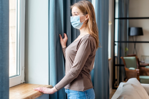 Frau mit Maske in Quarantäne, die die Fenster betrachtet