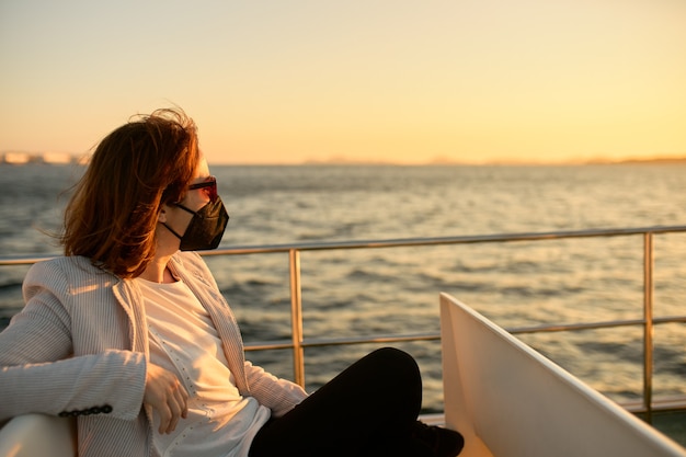 Frau mit Maske und Sonnenbrille auf einem Pendlerboot bei Sonnenuntergang.