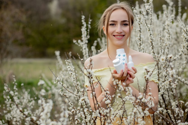 Frau mit Medizin in den Händen Fighting Spring Allergies Outdoor - Porträt einer allergischen Frau, umgeben von saisonalen Blumen